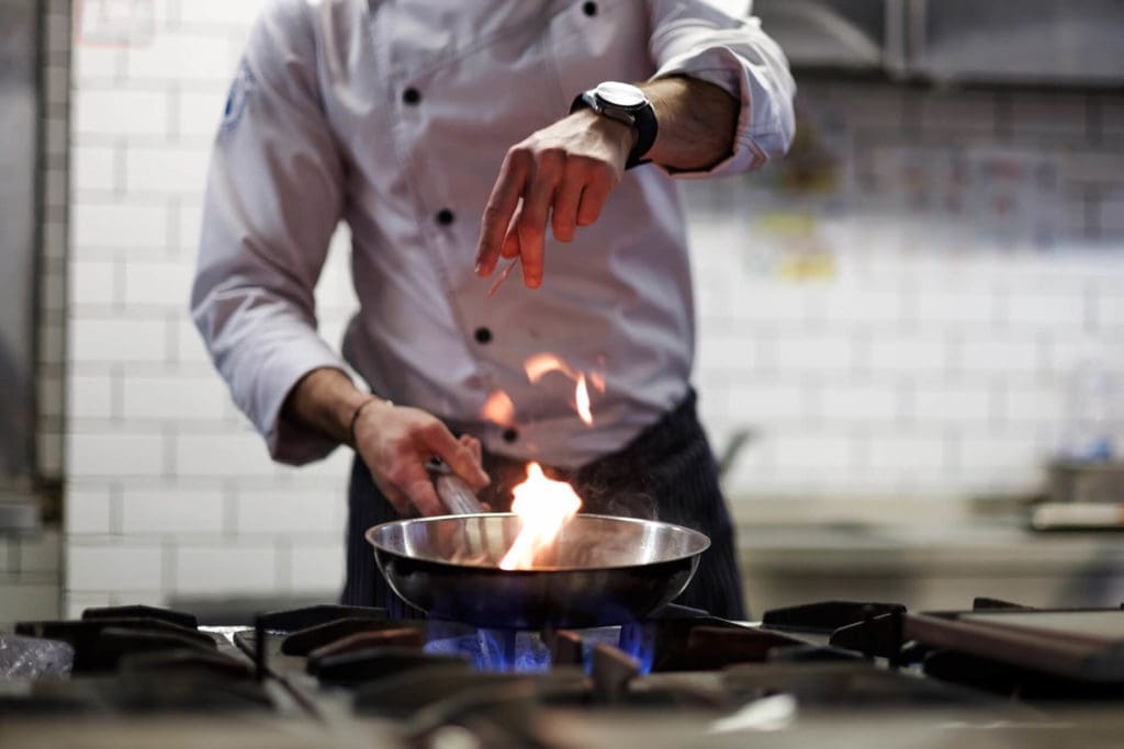 A chef pan frying food over a kitchen fire